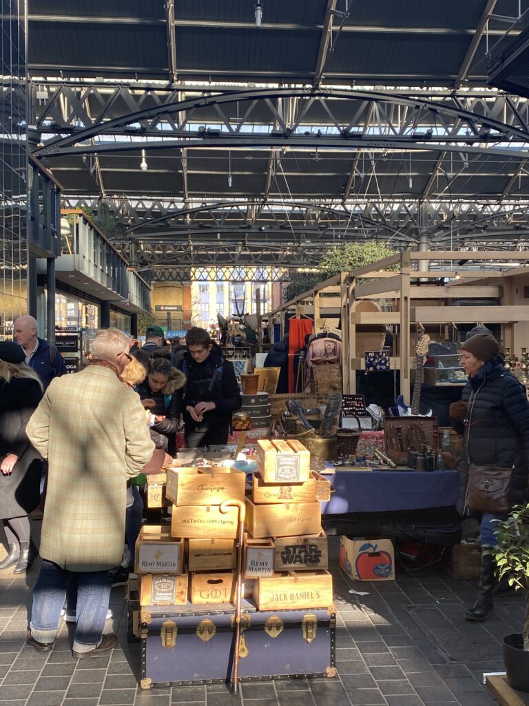 Shoppers browsing vintage trunks, wooden crates and antique goods under the covered arcade at Portobello Road Market
