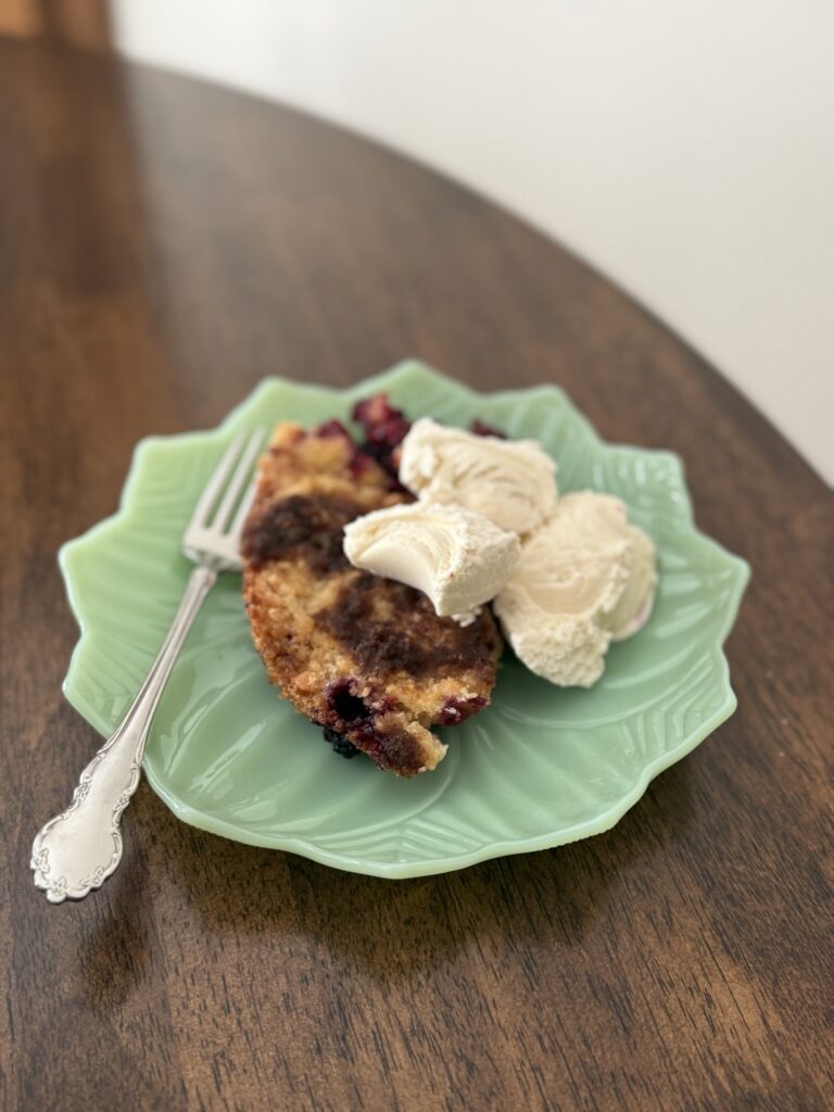 Serving of blackberry crumble topped with whipped cream on a green plate