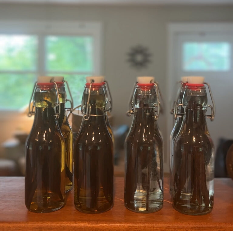Four swing top bottles of homemade vanilla extract lined up on a windowsill