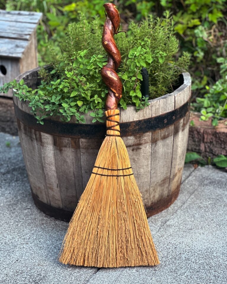 Half whiskey barrel planter full of oregano, mint and rosemary with a handmade broom leaning against it