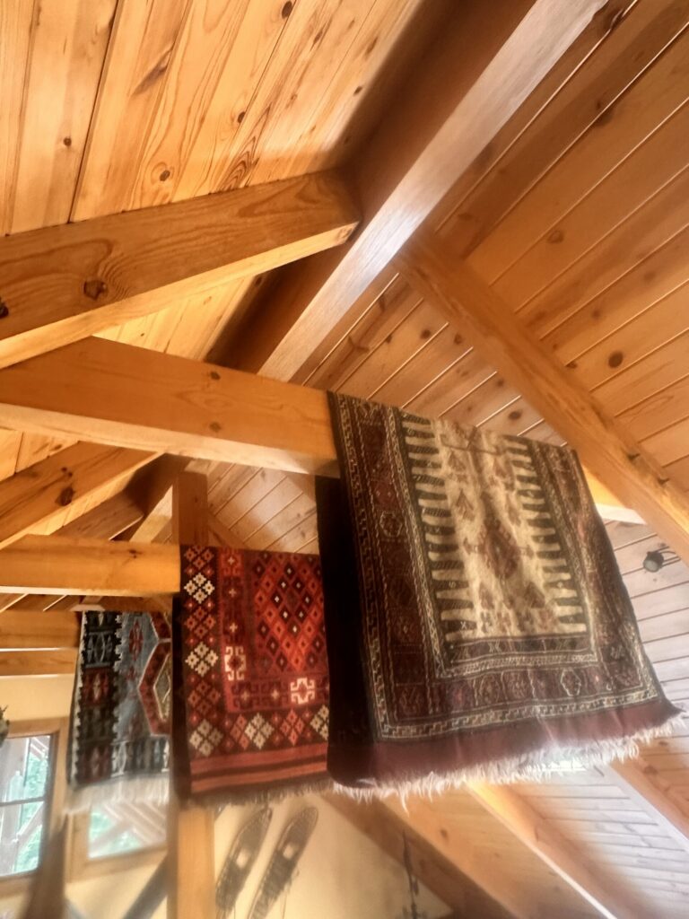 Vaulted cedar ceiling with exposed beams and a patterned rug on the wall