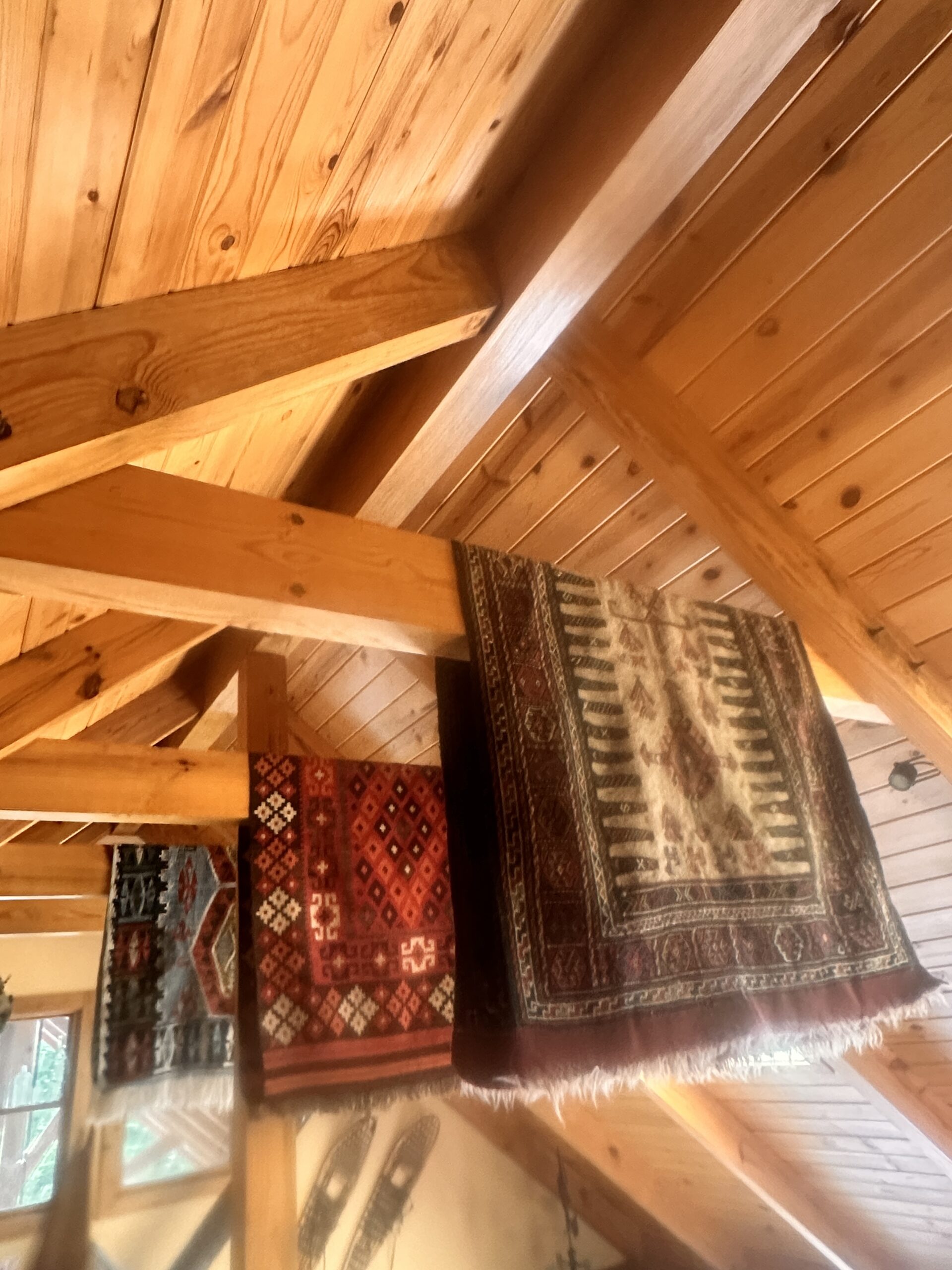Vaulted cedar ceiling with exposed beams and a patterned rug on the wall