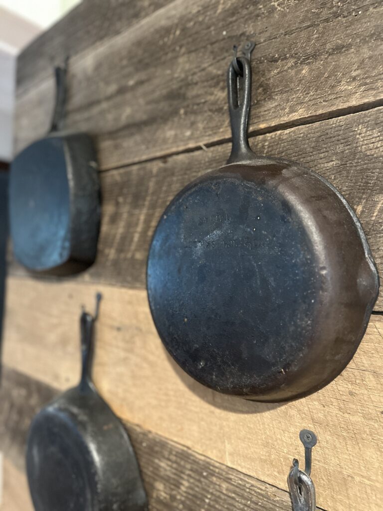 Close up of a reseasoned cast iron skillet hanging on a hook against reclaimed wood, maker marks visible on the base