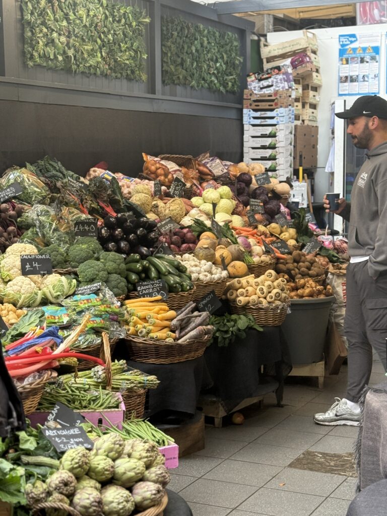Covered London market stall stacked with cauliflower, broccoli, aubergines, parsnips and potatoes in wicker baskets