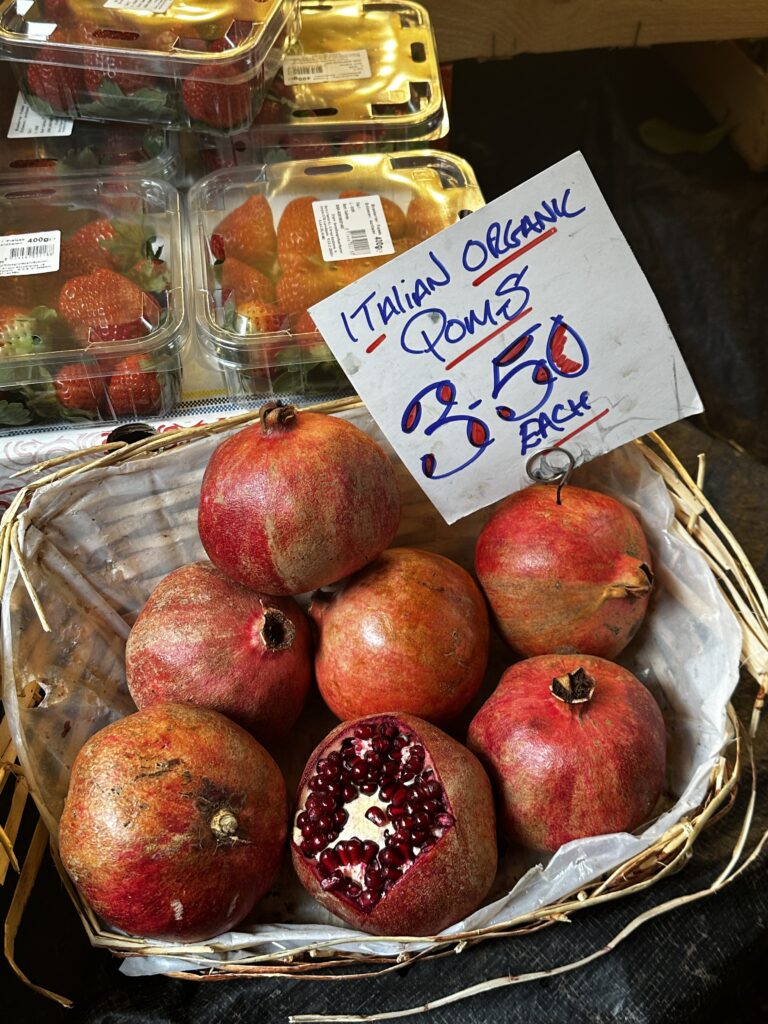 Basket of Italian organic pomegranates, one cut open to show the seeds, with a hand lettered price sign