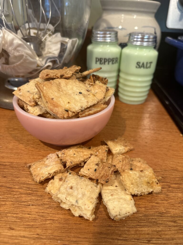 Bowl of crisp sourdough discard crackers with more scattered on the counter beside jadeite salt and pepper shakers