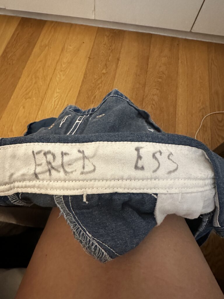 Inside waistband of vintage denim overalls with the name FRED ESS hand written in faded ink on the white twill tape