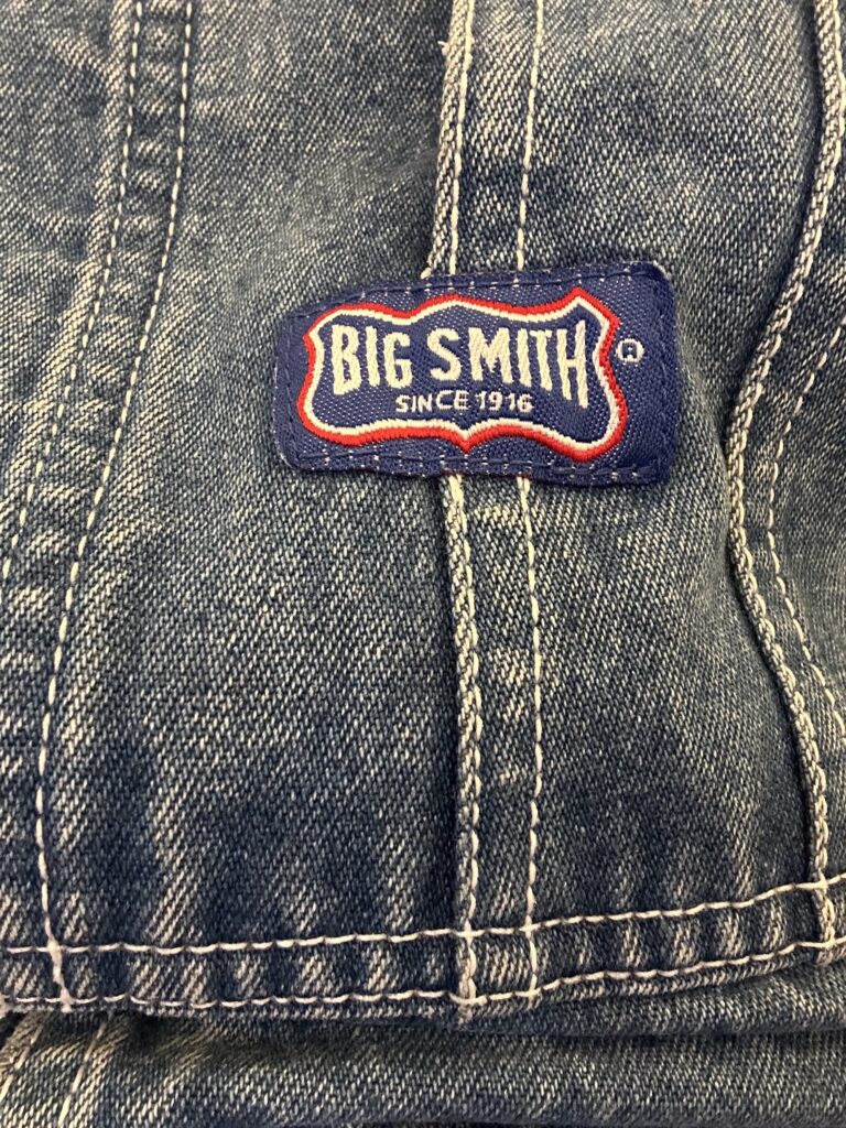 Big Smith Since 1916 woven label stitched to the bib of worn blue denim overalls