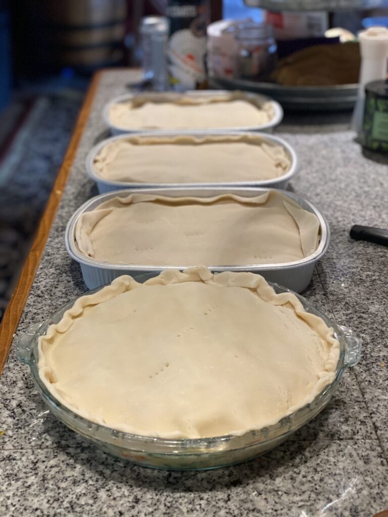 Four homemade turkey pot pies with crimped top crusts lined up on the counter waiting to go in the oven