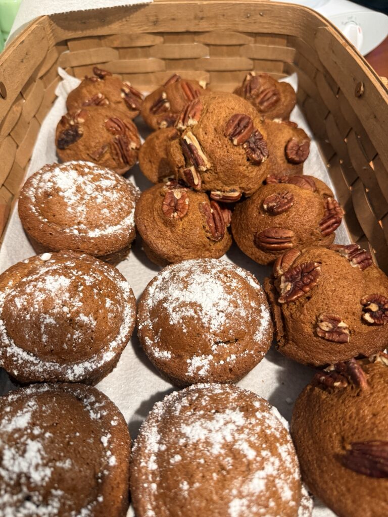 A basket of pumpkin muffins, some topped with pecans and some dusted with powdered sugar