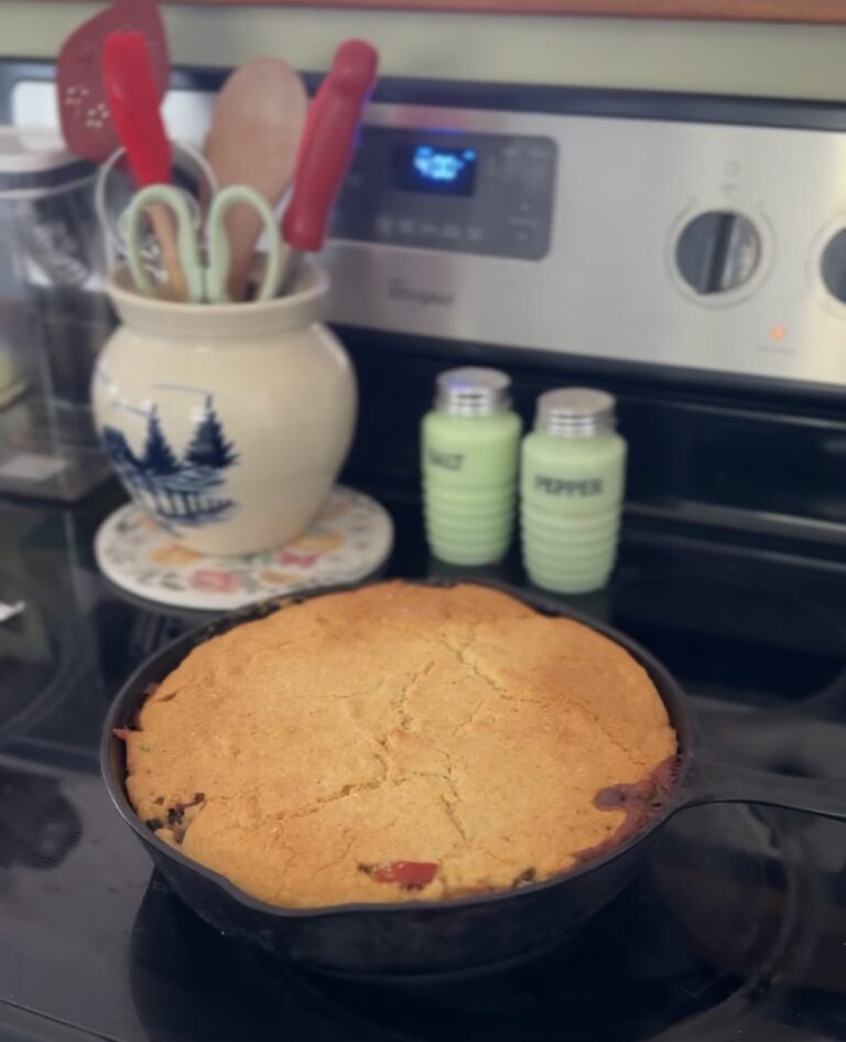 Cast iron skillet of cornbread topped chicken and kielbasa on the stovetop