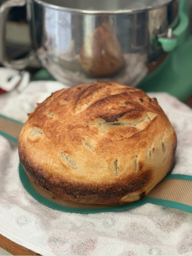 Round sourdough loaf with a golden crust cooling on a plate in the kitchen