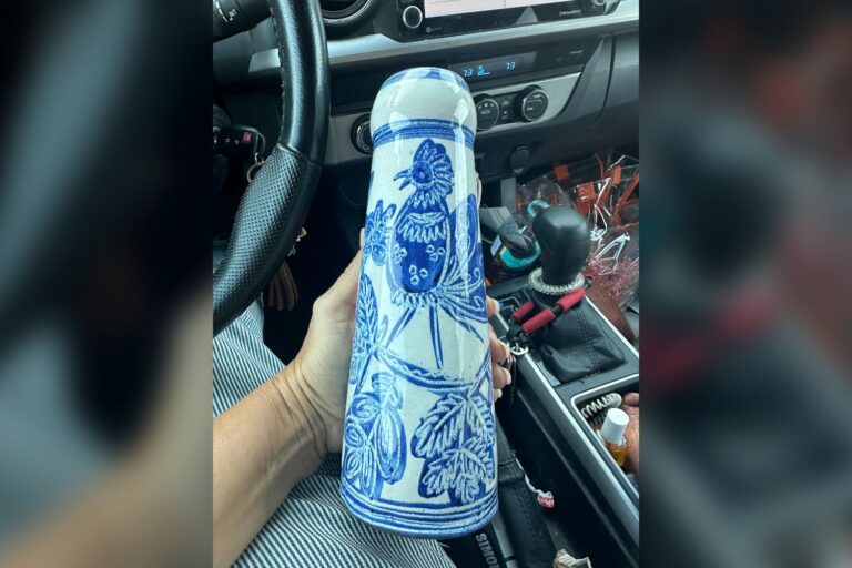 A tall blue and white Art Nouveau style vase with a bird design, held up in the car after a thrift store find