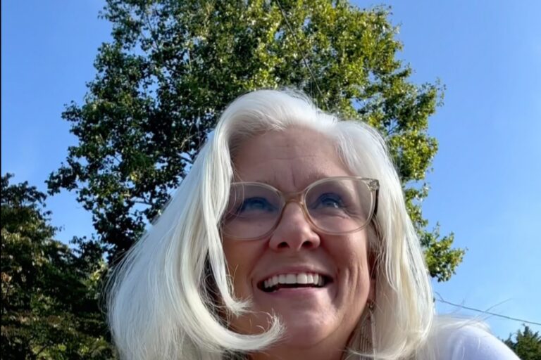 Jules Morris smiling up at the sky with green trees behind her