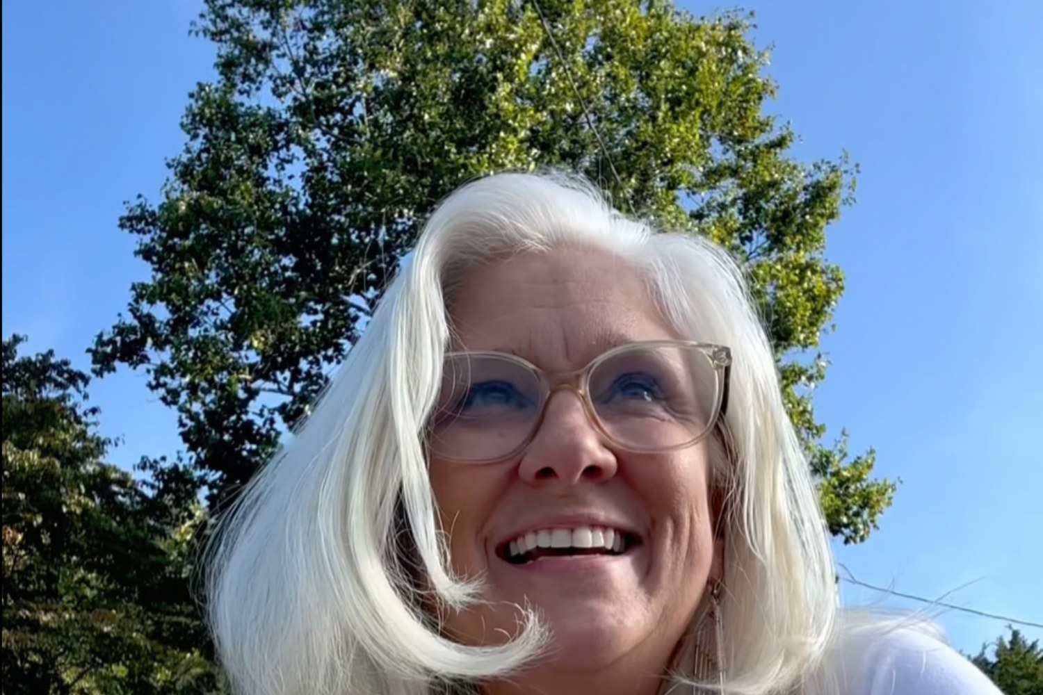 Jules Morris smiling up at the sky with green trees behind her
